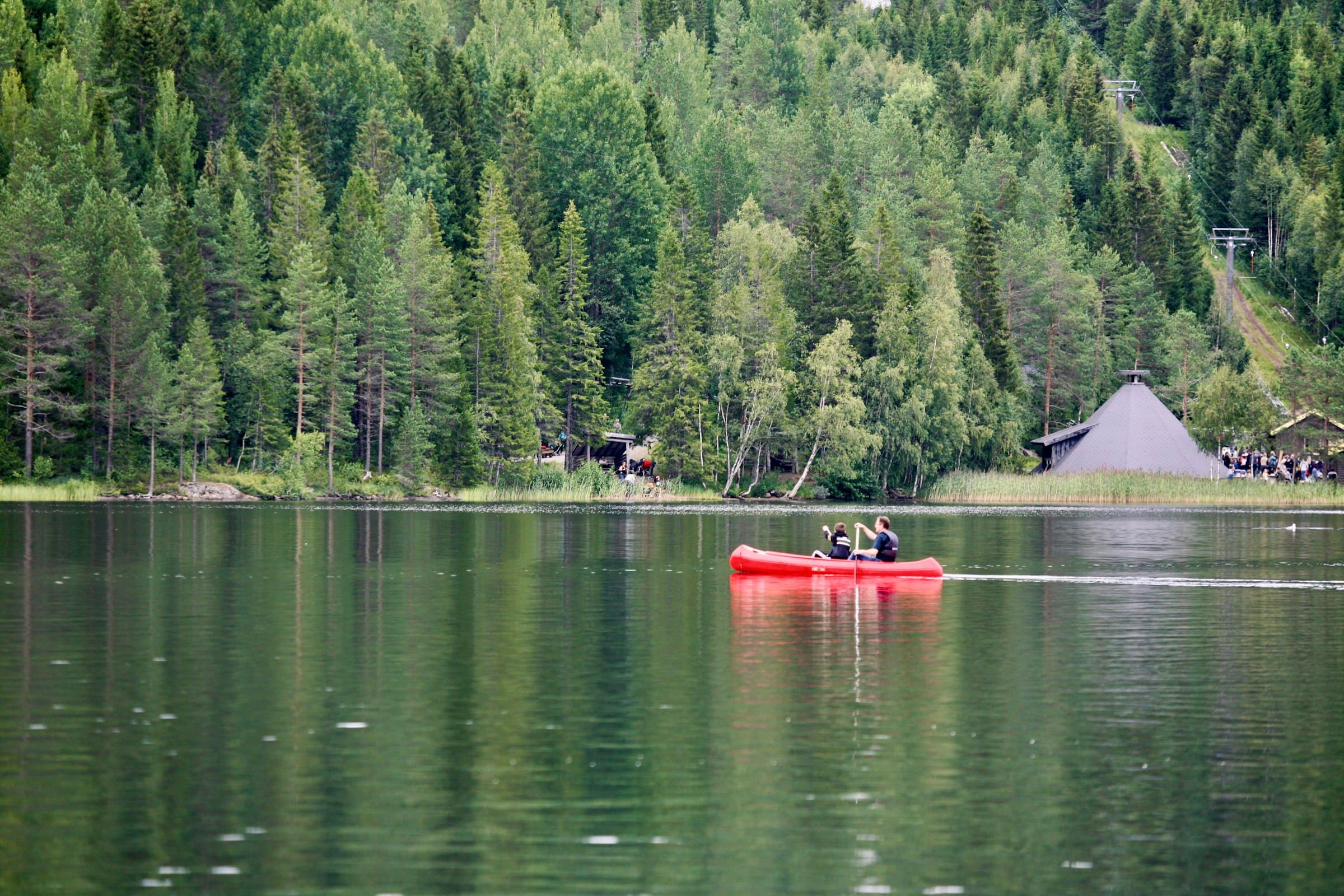 Zwei Menschen paddeln in einem roten Kanu über einen stillen Waldsee