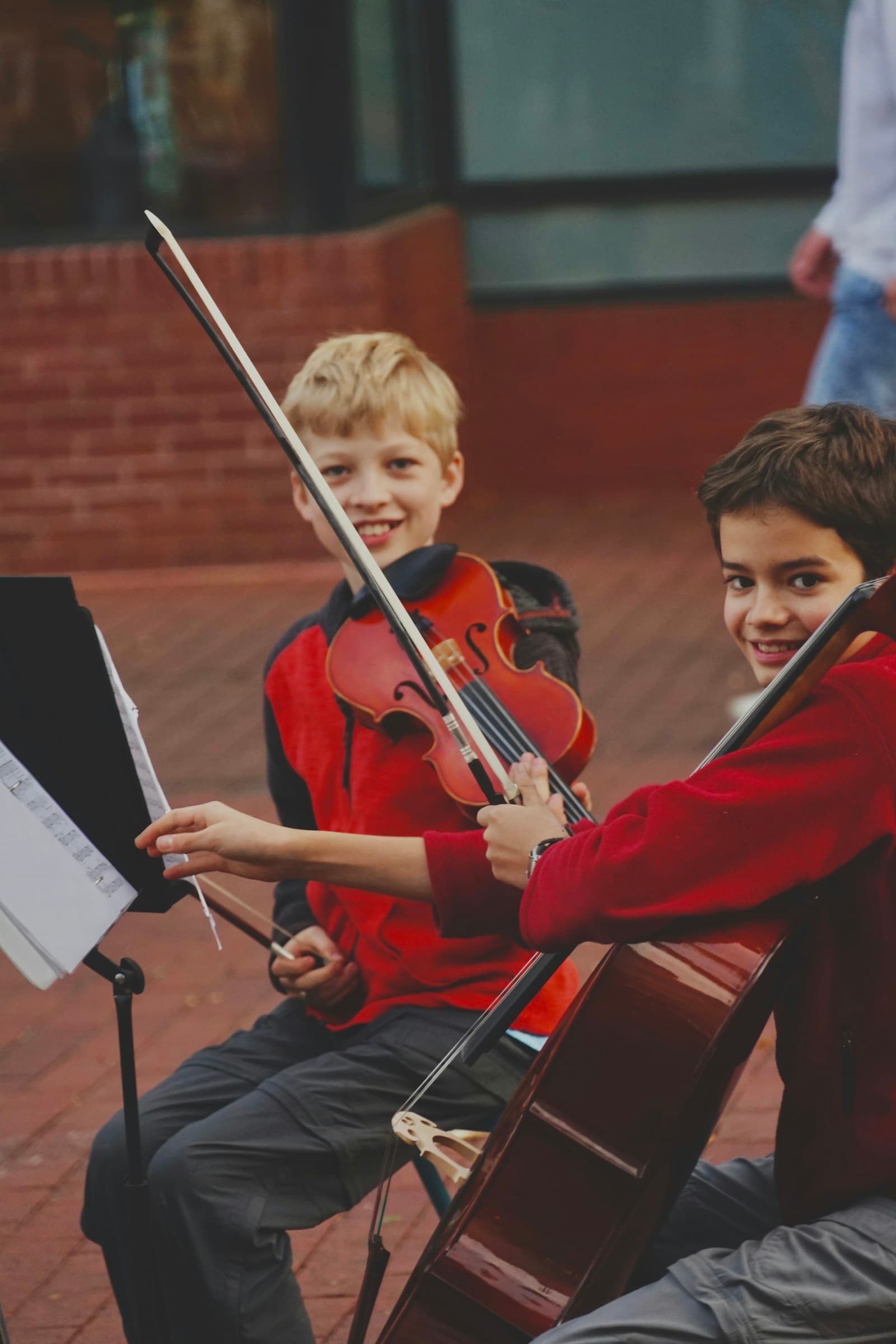 Zwei Jungen mit Geige und Cello lachen beim gemeinsamen Musizieren